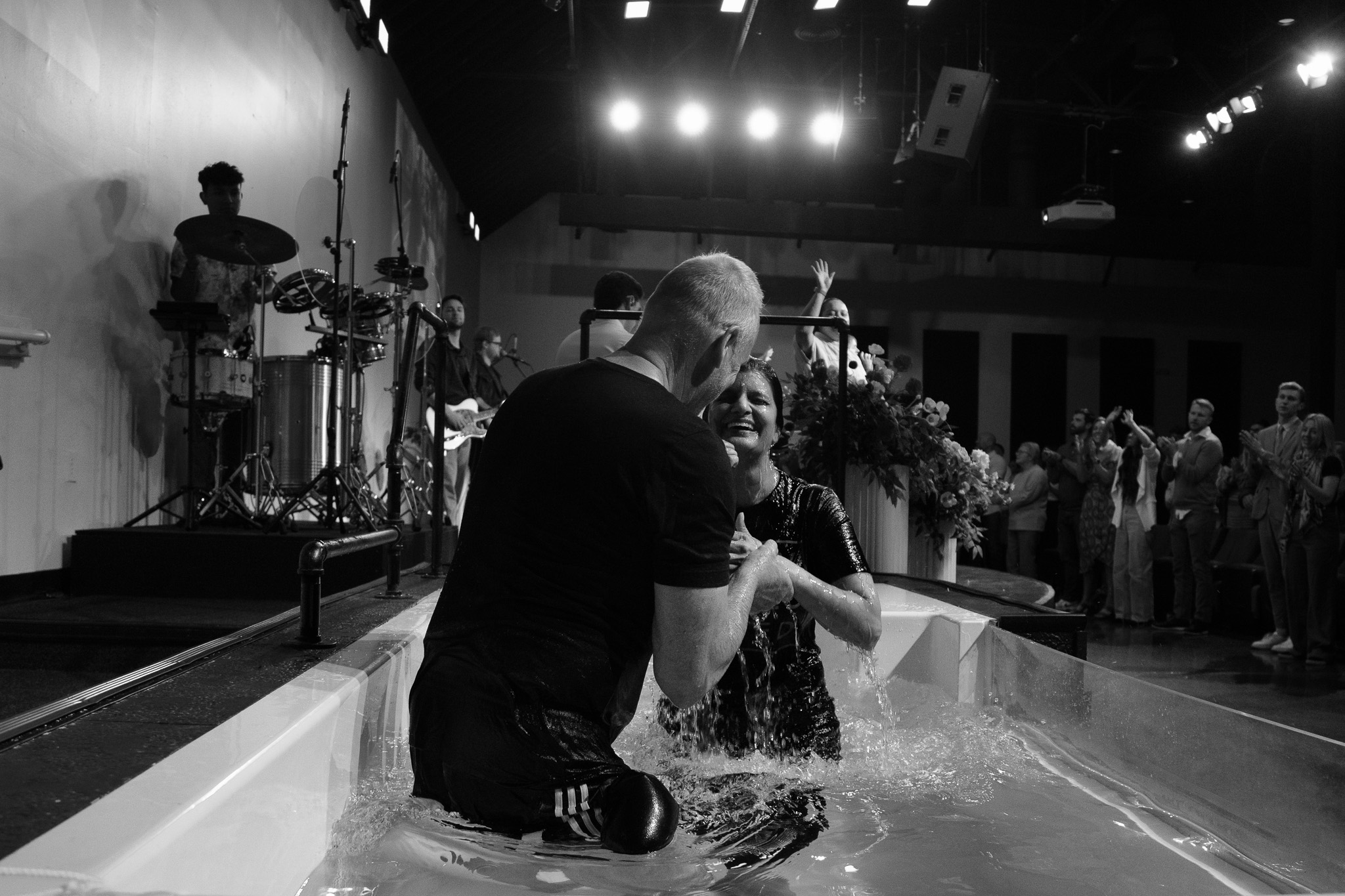A woman celebrates her baptism with a pastor as the congregation applauds