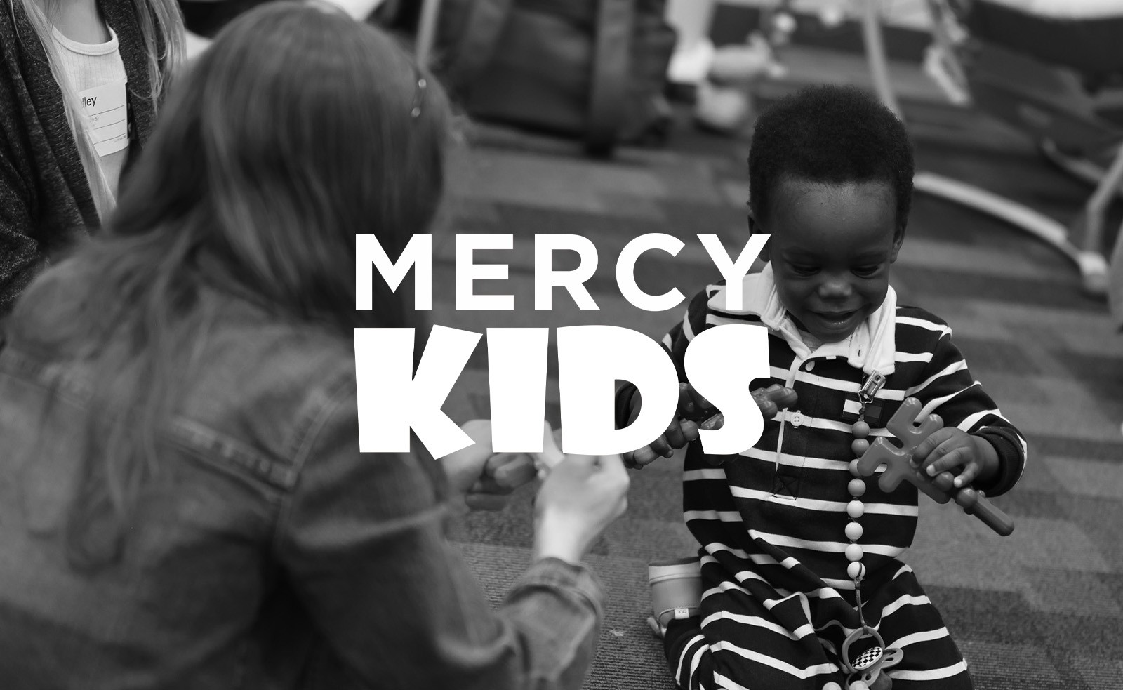 Mercy Kids logo over a photo of a child and a volunteer