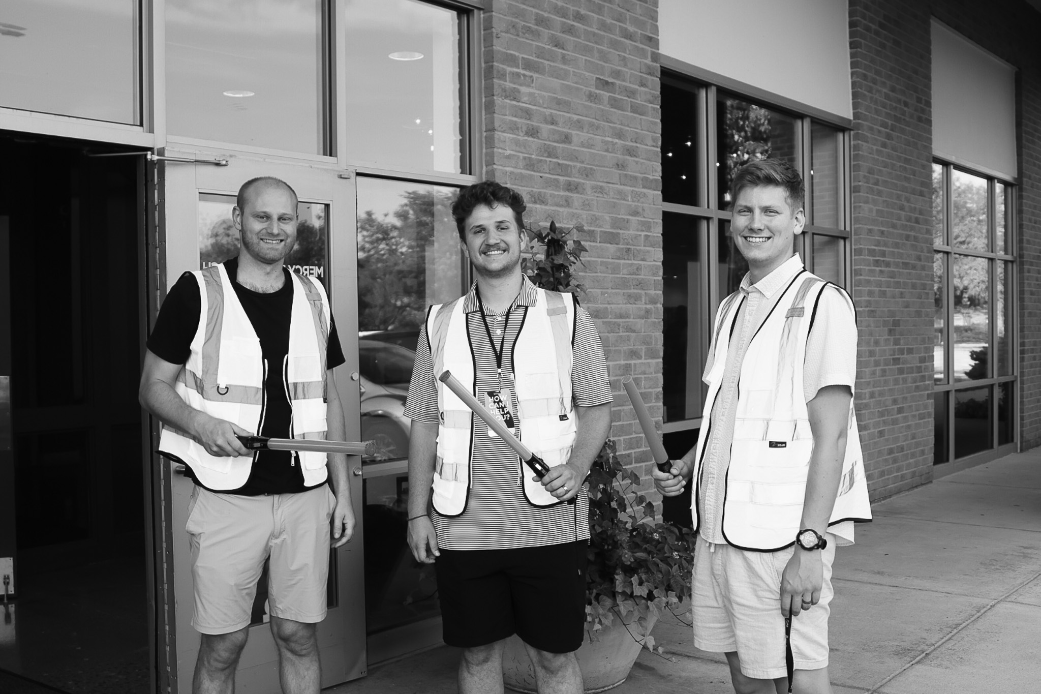 Three parking volunteers wearing safety vests and holding traffic wands outside the church